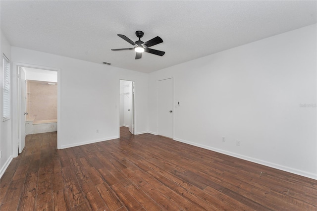 unfurnished bedroom featuring ceiling fan, ensuite bath, a spacious closet, dark wood-type flooring, and a closet