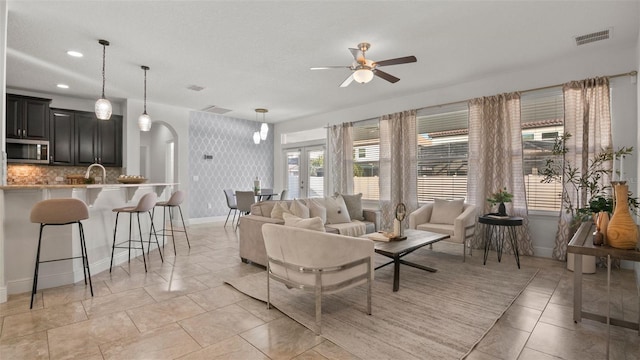 tiled living room featuring sink, ceiling fan, and french doors