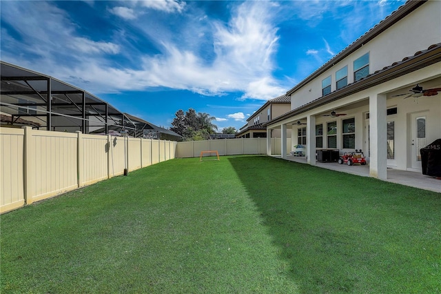 view of yard featuring ceiling fan, glass enclosure, and a patio area