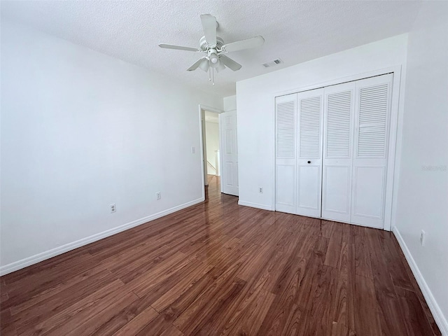 unfurnished bedroom featuring ceiling fan, a closet, dark hardwood / wood-style flooring, and a textured ceiling