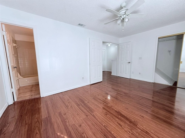 unfurnished bedroom featuring hardwood / wood-style floors, ceiling fan, connected bathroom, a closet, and a textured ceiling