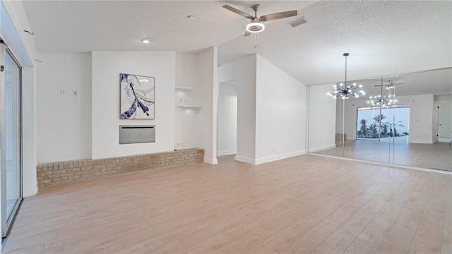 unfurnished living room featuring vaulted ceiling, a fireplace, a textured ceiling, ceiling fan with notable chandelier, and light hardwood / wood-style flooring