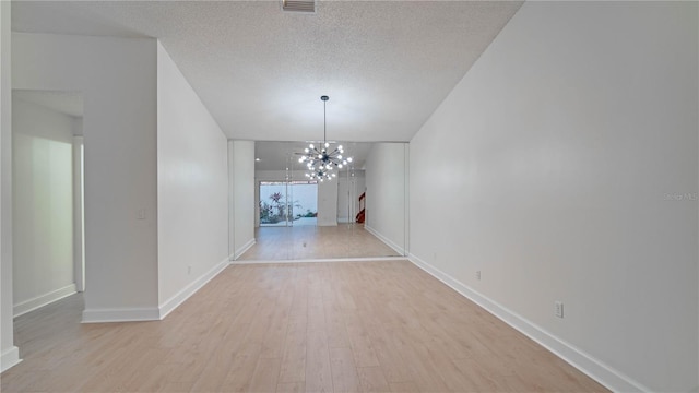 unfurnished dining area with an inviting chandelier, a textured ceiling, and light hardwood / wood-style floors