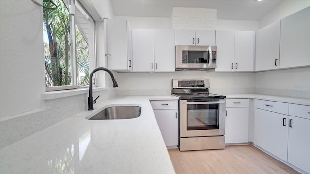 kitchen with white cabinets, sink, stainless steel appliances, and light hardwood / wood-style flooring