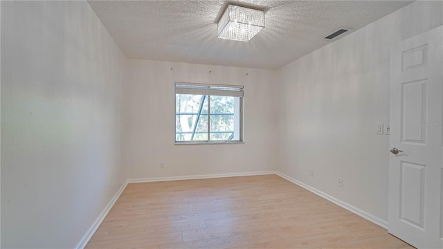 unfurnished room featuring a textured ceiling, an inviting chandelier, and light hardwood / wood-style floors