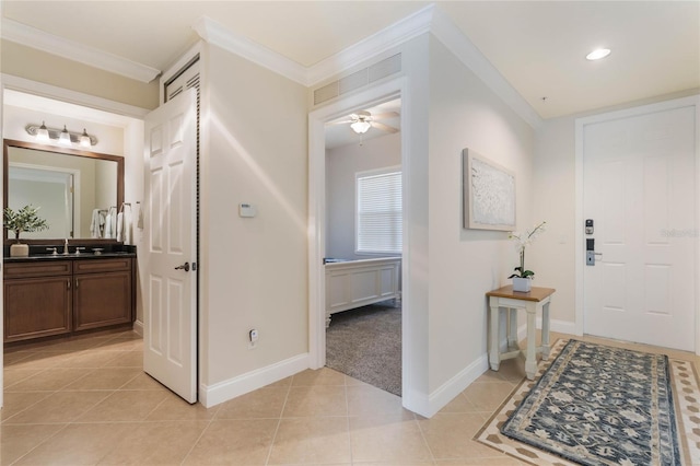 tiled foyer with ceiling fan, sink, and crown molding