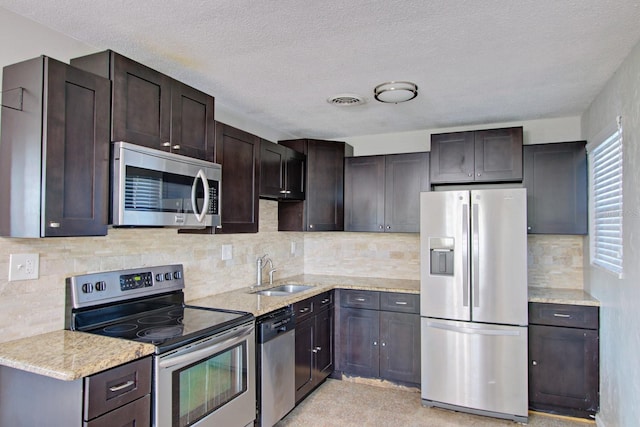 kitchen with appliances with stainless steel finishes, dark brown cabinets, a textured ceiling, light stone counters, and sink