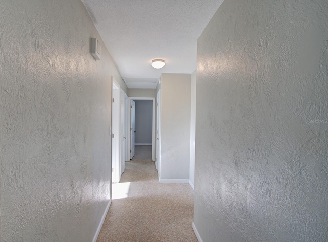 corridor with a textured ceiling and light colored carpet