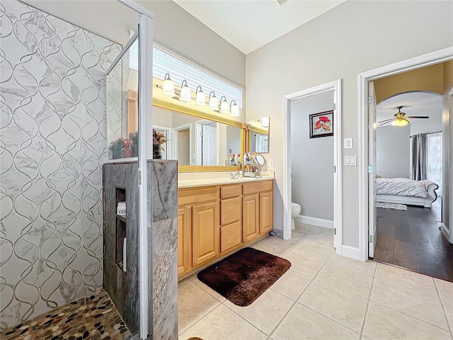 bathroom featuring tile patterned flooring, vanity, tiled shower, ceiling fan, and toilet