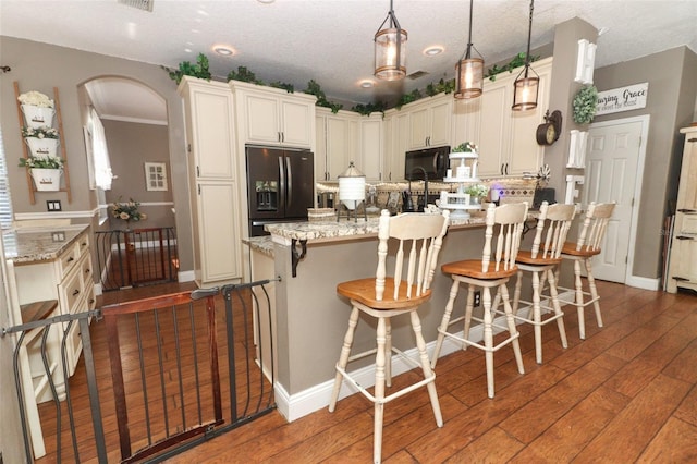 kitchen with pendant lighting, black appliances, a breakfast bar, light stone countertops, and cream cabinetry