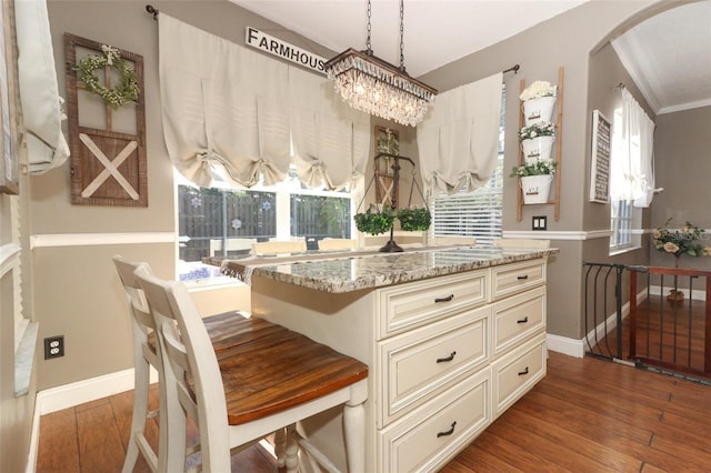 kitchen with dark wood-type flooring, hanging light fixtures, light stone countertops, a kitchen island, and cream cabinets