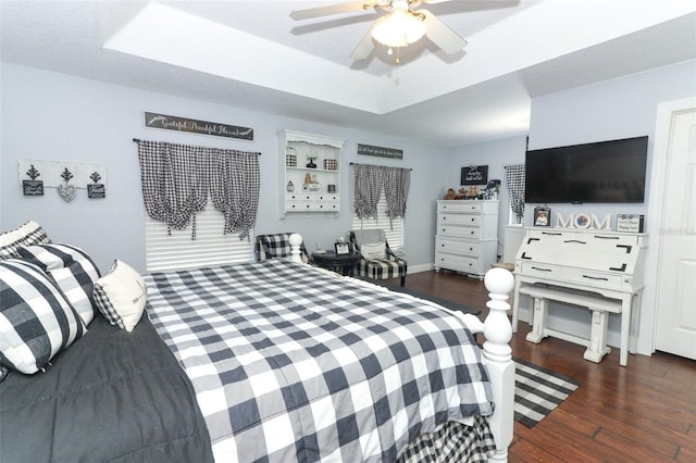 bedroom with ceiling fan, a tray ceiling, and dark hardwood / wood-style floors