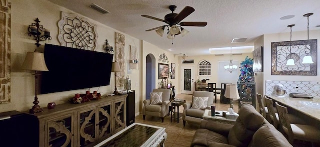 living room with tile patterned flooring, ceiling fan with notable chandelier, and a textured ceiling