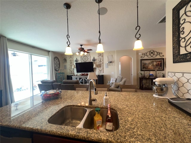 kitchen featuring sink, stone countertops, decorative light fixtures, a textured ceiling, and ceiling fan