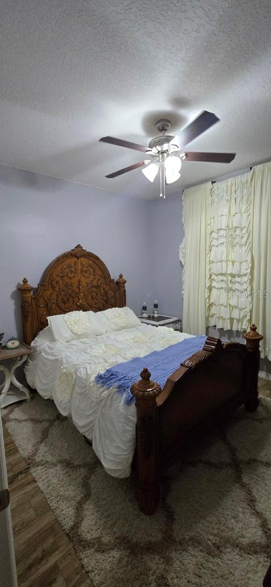 bedroom featuring dark hardwood / wood-style flooring, ceiling fan, and a textured ceiling