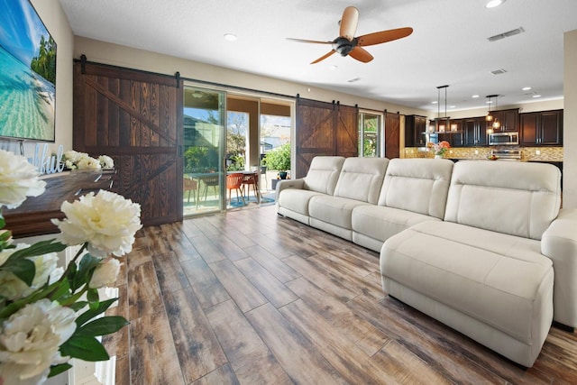 living room with a barn door, hardwood / wood-style floors, and ceiling fan