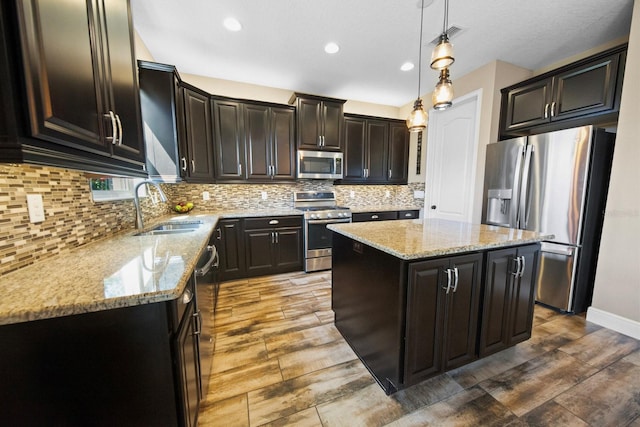 kitchen with sink, hanging light fixtures, stainless steel appliances, a center island, and tasteful backsplash