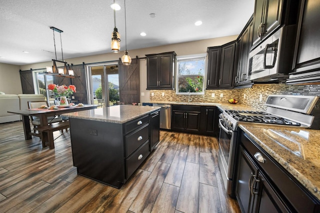 kitchen with decorative light fixtures, appliances with stainless steel finishes, a kitchen island, a barn door, and washing machine and dryer