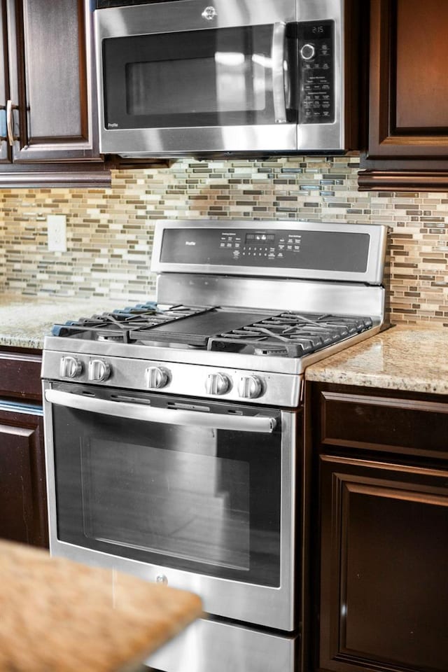 kitchen featuring light stone counters, decorative backsplash, dark brown cabinets, and appliances with stainless steel finishes