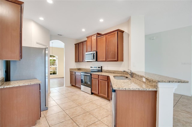 kitchen with light stone countertops, appliances with stainless steel finishes, sink, a kitchen breakfast bar, and kitchen peninsula