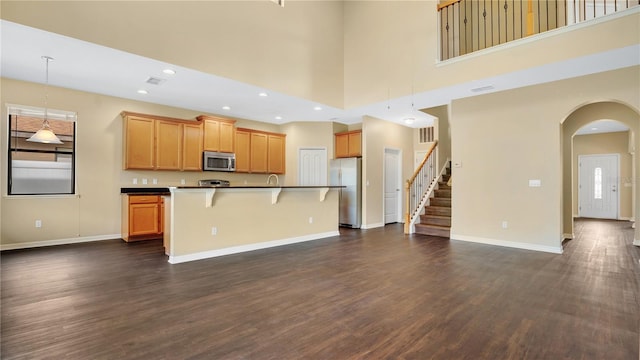 kitchen with hanging light fixtures, appliances with stainless steel finishes, a towering ceiling, and an island with sink