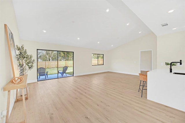 unfurnished living room featuring high vaulted ceiling, sink, and light hardwood / wood-style flooring