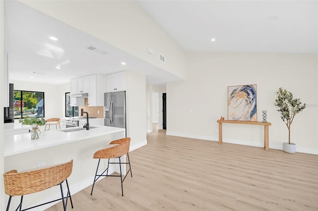 kitchen featuring sink, stainless steel fridge, a breakfast bar area, light hardwood / wood-style flooring, and white cabinetry