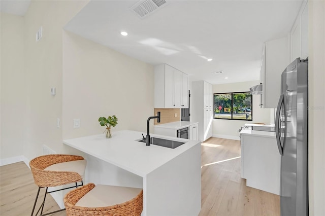 kitchen with sink, white cabinets, stainless steel fridge, kitchen peninsula, and light wood-type flooring