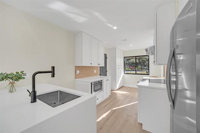 kitchen featuring sink, white cabinetry, stainless steel appliances, light hardwood / wood-style floors, and decorative backsplash