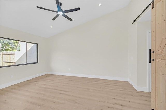 spare room featuring ceiling fan, a barn door, and light hardwood / wood-style floors