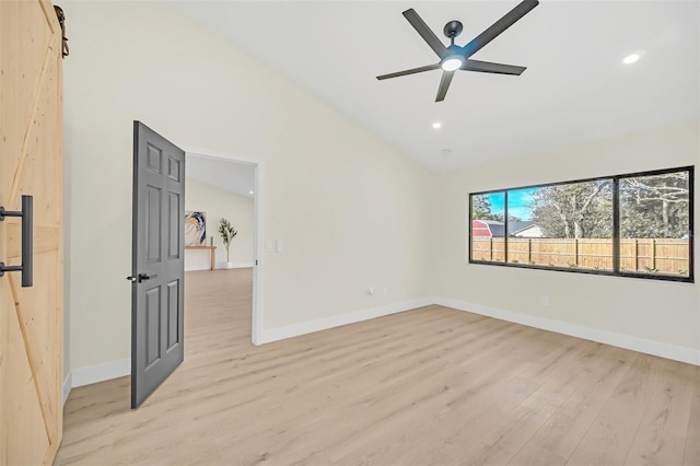 unfurnished room with ceiling fan, a barn door, high vaulted ceiling, and light hardwood / wood-style floors