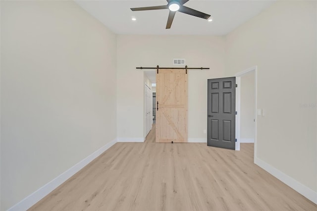 unfurnished room featuring a towering ceiling, light hardwood / wood-style floors, a barn door, and ceiling fan