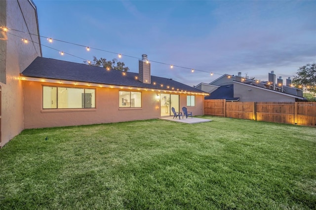 back house at dusk with a patio and a lawn