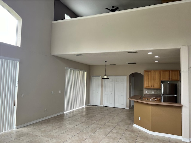 kitchen with light tile patterned floors, tasteful backsplash, a towering ceiling, hanging light fixtures, and stainless steel refrigerator