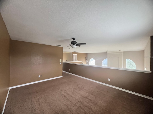 spare room featuring ceiling fan, a wealth of natural light, and dark colored carpet