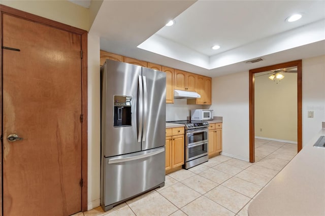 kitchen featuring ceiling fan, light tile patterned flooring, a tray ceiling, stainless steel appliances, and light brown cabinetry