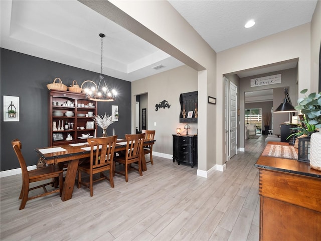 dining space with light wood-type flooring, a chandelier, a textured ceiling, and a raised ceiling