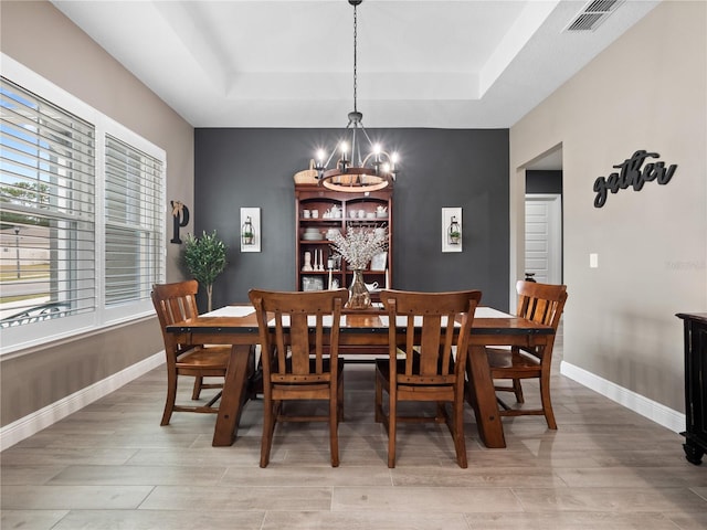 dining room featuring a raised ceiling, light hardwood / wood-style flooring, and a notable chandelier