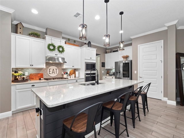 kitchen with pendant lighting, a center island with sink, sink, stainless steel appliances, and white cabinets