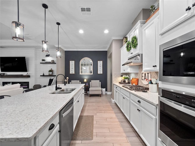 kitchen with white cabinetry, an island with sink, stainless steel appliances, decorative light fixtures, and sink