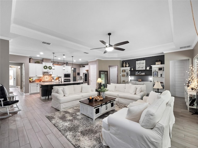 living room featuring ceiling fan, ornamental molding, a raised ceiling, and sink