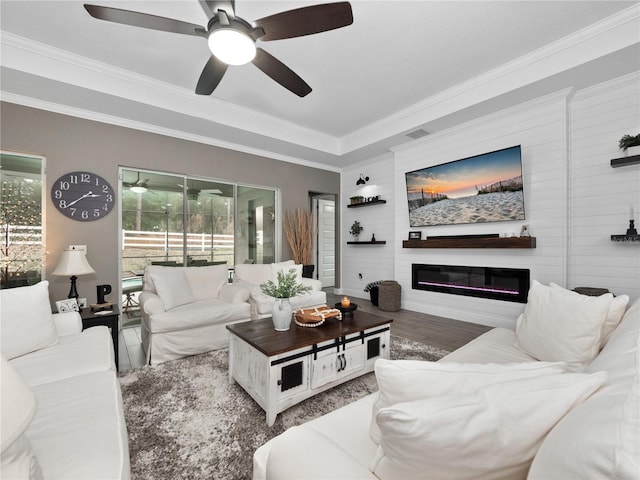 living room with ceiling fan, a large fireplace, crown molding, and hardwood / wood-style floors