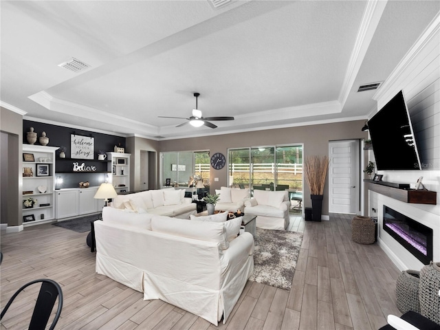 living room featuring ceiling fan, crown molding, light hardwood / wood-style floors, and a tray ceiling