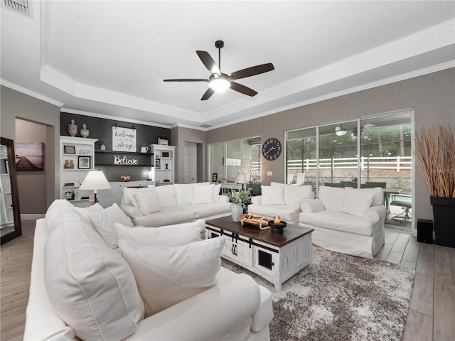 living room featuring ceiling fan, a tray ceiling, ornamental molding, and light wood-type flooring