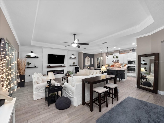 living room with ceiling fan, light wood-type flooring, a fireplace, and a tray ceiling