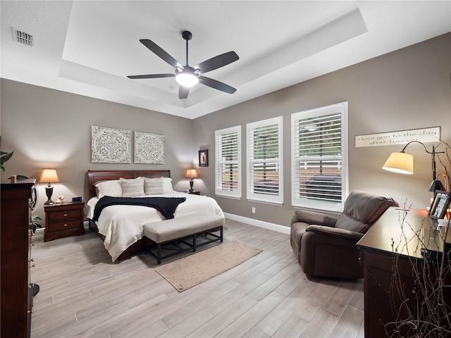 bedroom featuring light wood-type flooring, ceiling fan, and a tray ceiling