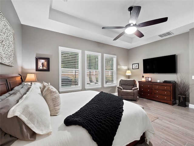 bedroom with a raised ceiling, ceiling fan, and light hardwood / wood-style flooring