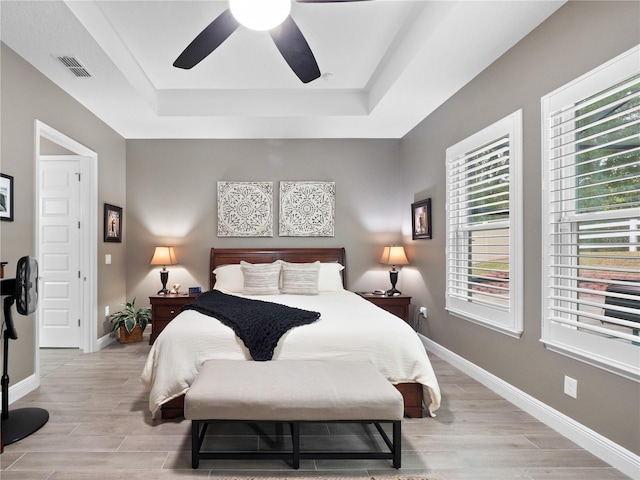 bedroom featuring light wood-type flooring, ceiling fan, and a tray ceiling