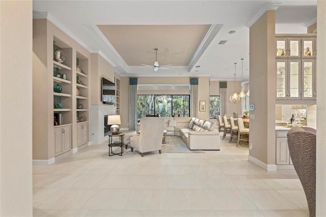 living room with ceiling fan with notable chandelier, built in shelves, ornamental molding, a raised ceiling, and light tile patterned floors