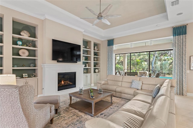 living room featuring ceiling fan, crown molding, a raised ceiling, and built in shelves